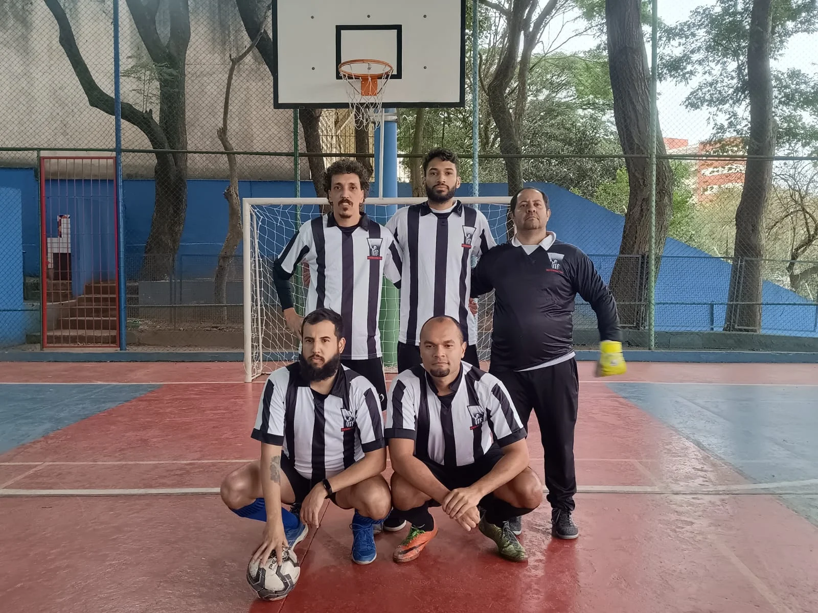 Cinco homens posando com uniforme esportivo listrado em preto e branco na quadra de esportes.